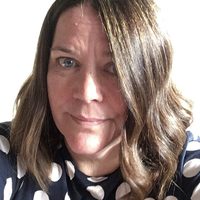 Maureen wears a polka dot top. She has brown hair which stylishly covers her left eye.