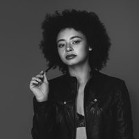Black and white image of Nicolette, she has an afro and leather jacket.