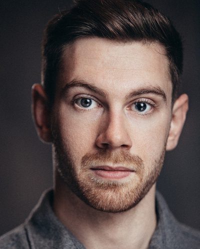 Robin looks at the camera, he wears a grey shirt and the background is also grey