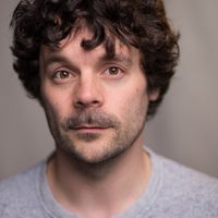 Ross Mann looks at the camera, he has fluffy brown hair.