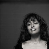 Black and white image of Uma, she has curly hair and holds a powerful gaze.