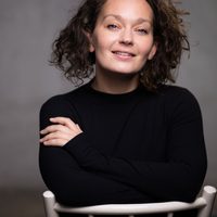 Vicki sits on a chair with her arms crossed. She smiles at the camera.