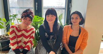 The three fellows, Andrea Ling, Hannah Low, and Leah Byrne, sit in front of a window and smile happily at the camera