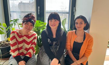 The three fellows sit by a window and smile happily at the camera