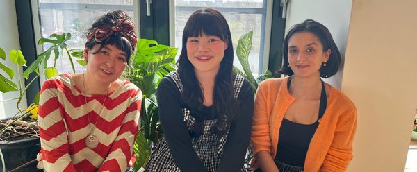 The three fellows, Andrea Ling, Hannah Low, and Leah Byrne, sit in front of a window and smile happily at the camera