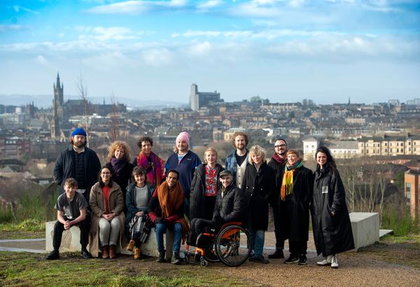 A group of artists stood at the viewing point at the Glasgow Claypits, with a blue sky and the Glasgow skyline behind them.