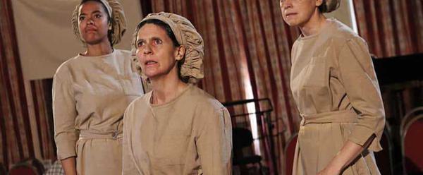 Three women dressed in factory overalls and bonnets look worried