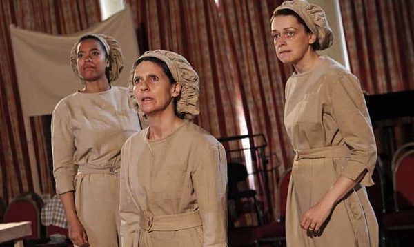 Three women dressed in factory overalls and bonnets look worried