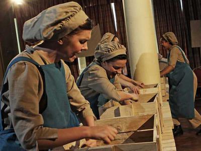 Women in factory clothing pack boxes in a line