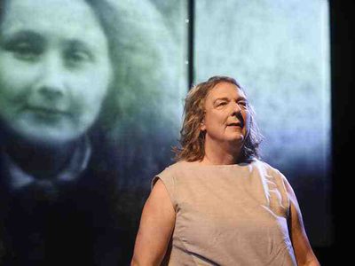 A grey-haired woman in a grey dress stands