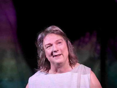 woman with shoulder length grey hair in a grey dress is smiling