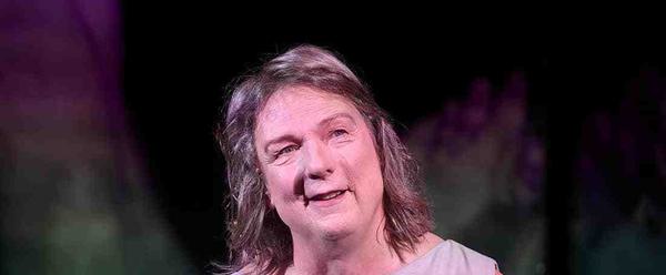 woman with shoulder length grey hair in a grey dress is smiling