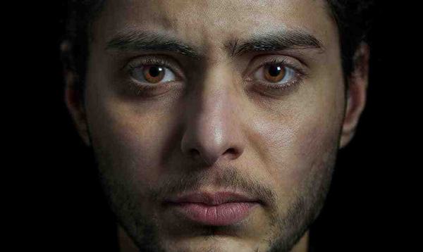 A young man with dark hair and light brown eyes looks forward, directly into the camera.