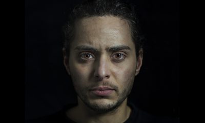A young man with dark hair and light brown eyes looks forward, directly into the camera.