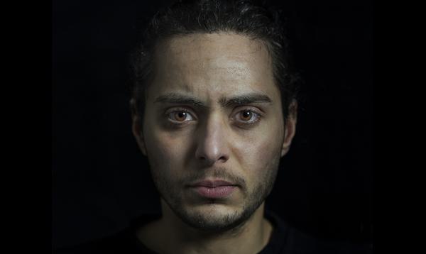 A young man with dark hair and light brown eyes looks forward, directly into the camera.