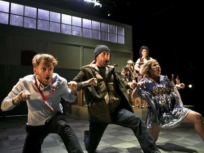 Three actors on bended knee, mid-song making a rowing motion with their hands.