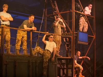 A group of men strike various poses atop some scaffolding
