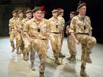 A group of actors in military uniform march with their knees high