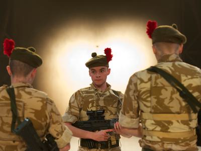 An actor dressed as a soldier stands with his gun in his hands, facing two other men