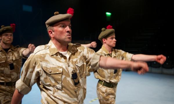 Three actors in military uniform march with their arms outstretched