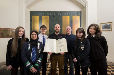 A group of school children and two staff members stand around a record of the real Black-Watch