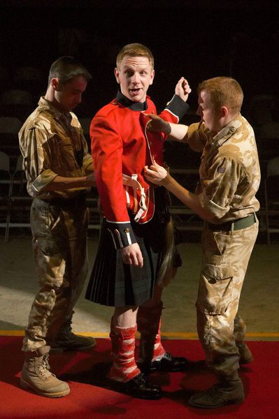A man is dressed in Scottish military attire by two other soldiers