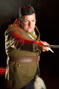 An actor in military attire thrusts forward with a large sword