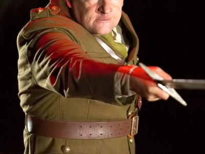 An actor in military attire thrusts forward with a large sword