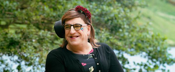 A woman is sat in an electric wheelchair in front of a lake