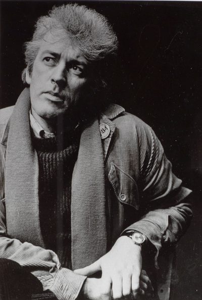 A black and white photo of a man sitting down, with his left arm propped up as he looks off to his right.