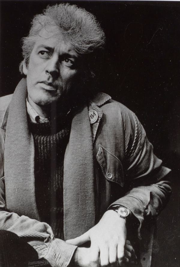 A black and white photo of a man sitting down, with his left arm propped up as he looks off to his right.