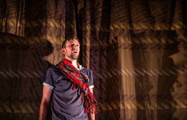 Calum MacDonald wearing a tshirt and a red tartan scarf stands on the left hand side of the image.