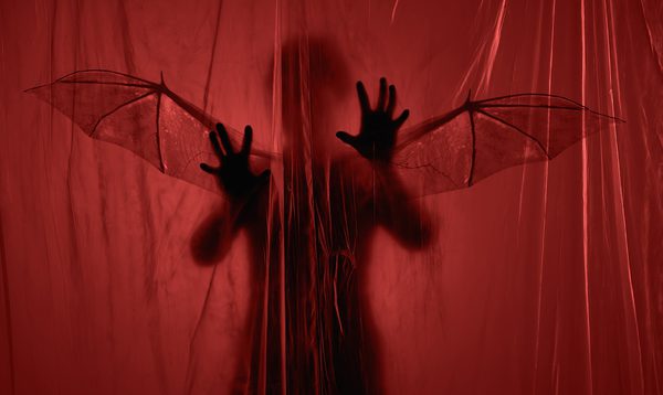 A shadowy figure with bat wings lurks behind a red translucent curtain
