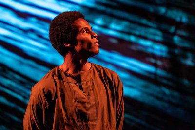 An actor stands illuminated against a projected backdrop