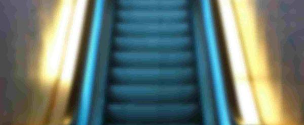 A figure sits on an escalator. The escalator is illuminated in blue and yellow light.