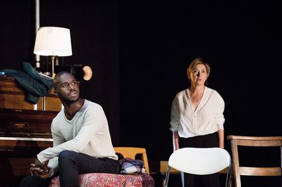 Thierry Mabonga and Isabelle Vincent in First Snow / Premiere Neige. Thierry sits on the left of the screen beside a piano, staring into the distance. Isabelle stands slightly out of focus behind him, also staring off into the distance.