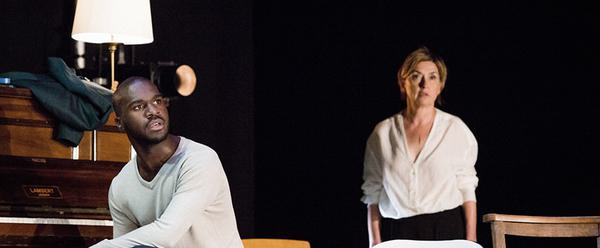 Thierry Mabonga and Isabelle Vincent in First Snow / Premiere Neige. Thierry sits on the left of the screen beside a piano, staring into the distance. Isabelle stands slightly out of focus behind him, also staring off into the distance.