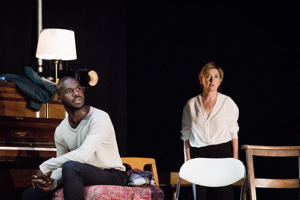 Thierry Mabonga and Isabelle Vincent in First Snow / Premiere Neige. Thierry sits on the left of the screen beside a piano, staring into the distance. Isabelle stands slightly out of focus behind him, also staring off into the distance.