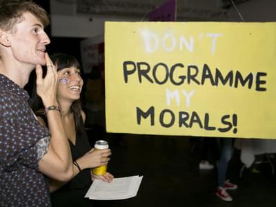 A man and a woman stand beside a sign that says "Don't programme my morals!"