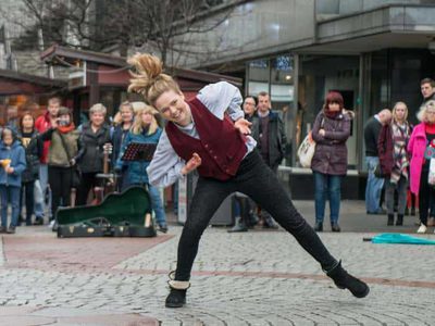 A young woman in a waistcoast, shirt and jeans dances in the street