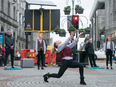 A young woman dances in the street with her arms out stretched to the sky