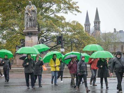 A group of people with green umbrellas walk across a street