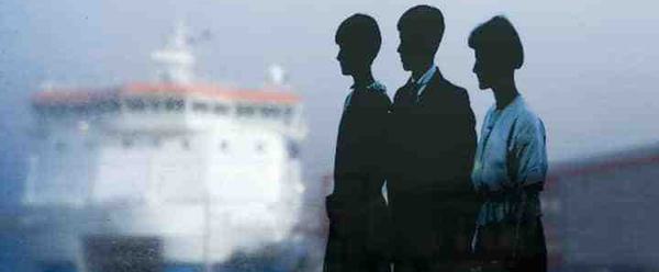 Three figures in silhouette appear in the foreground of the image. Behind them, a large white ferry has docked at a harbour.