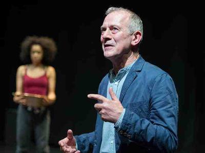 A middle aged grey-haired man explains something as a young woman looks on