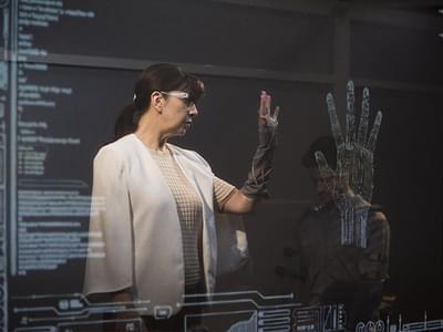A woman holds her hand up to a very large screen with a detailed diagram of a palm displayed on it
