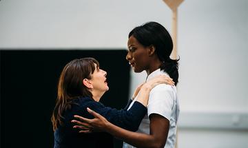 Two women holding one anothers shoulders and looking into one another's eyes.