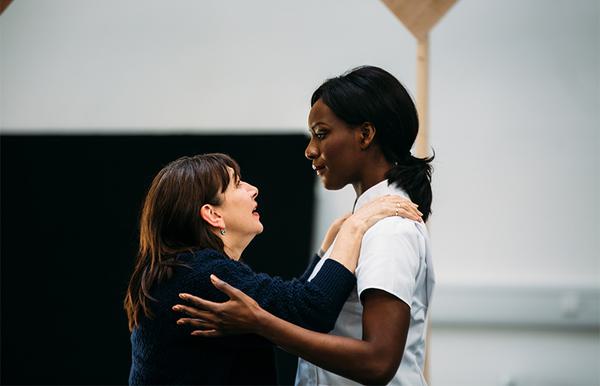 Two women holding one anothers shoulders and looking into one another's eyes.