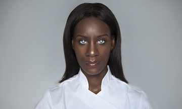 A young woman stares straight ahead with an expressionless look on her face. She has white rings around the iris of her eyes.