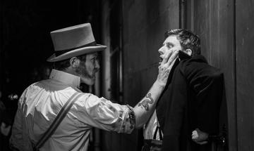 An actor with mutton chops and a top hat threatens another