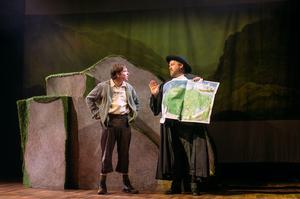 two men stand next to a boulder - man on right holds a map